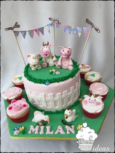 a birthday cake decorated with farm animals and cupcakes on a green platter