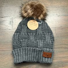 a gray hat with a brown pom - pom on it sitting on top of a wooden floor