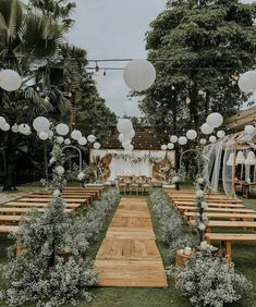 an outdoor wedding setup with wooden benches and white lanterns hanging from the ceiling, surrounded by greenery