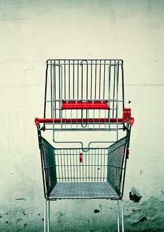 an empty shopping cart sitting in front of a white wall with red trim on it