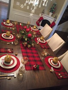 a dining room table set for christmas with red and black plaid placemats, silverware