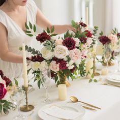 a woman setting a table with flowers and candles on the tables for an elegant dinner