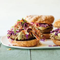 three burgers with coleslaw slaw on them sitting on a white plate