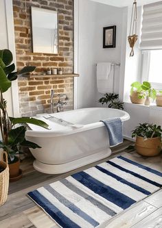 a white bath tub sitting in a bathroom next to a sink and window with potted plants