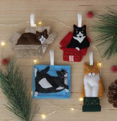 four felt ornaments with cats on them hanging from string and decorated pine cones in the background