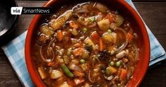 a red bowl filled with vegetable stew on top of a wooden table