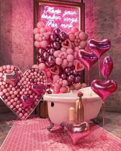 a bathtub filled with lots of pink balloons and heart shaped balloons in front of a sign