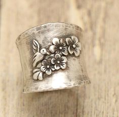 "This ring features cherry blossom flowers and a tiny little hummingbird. This is a wide .925 sterling silver band with a gently hammered texture. This wide band ring features .925 sterling silver trailing cherry blossoms and a tiny hummingbird ready to feed on nectar. You may choose this ring in polished silver or an oxidized silver that is hand buffed to show detail. Cherry blossom ring is made from .925 sterling silver and is great for the flower lover, those that love boho, hummingbird lover Cherry Blossom Ring, Wide Band Ring, Meaningful Jewelry, Wide Band Rings, Sterling Silver Bands, Wide Bands, Accessories Rings, Ring Sterling Silver, Ring For Women