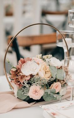 an arrangement of flowers and greenery in a basket on a table with wine glasses