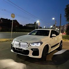 a white bmw x6 parked on the side of the road at night with street lights in the background