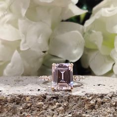 a pink diamond ring sitting on top of a rock next to white flowers and greenery