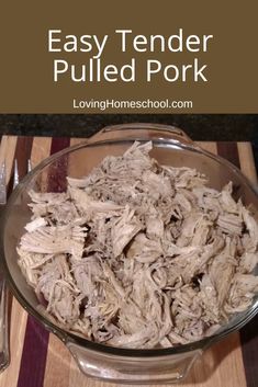 shredded pulled pork in a glass bowl on top of a cutting board next to a knife and fork