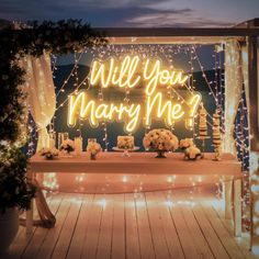 a lit up sign that says will you marry me? with flowers and candles around it