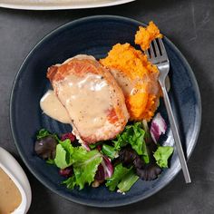 a blue plate topped with meat covered in gravy next to a salad and mashed potatoes