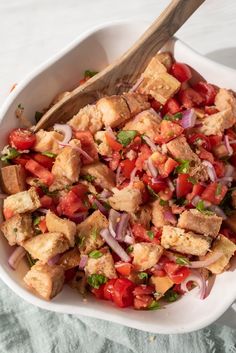 a white bowl filled with tofu and onions on top of a table next to a wooden spoon