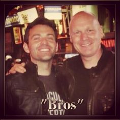 two men standing next to each other in front of a neon city sign with the words bros on it