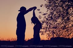 a man and woman standing next to each other in front of a tree at sunset