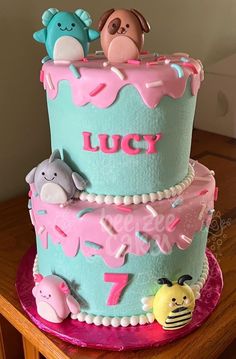 a three tiered cake with frosting and animals on it's sides, sitting on top of a wooden table