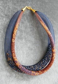 three necklaces with different colored beads on top of a gray carpeted floor next to a pair of scissors