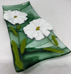 a green glass plate with two white flowers on the bottom and one flower in the middle