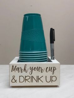 a stack of blue cups sitting on top of a wooden sign next to a marker