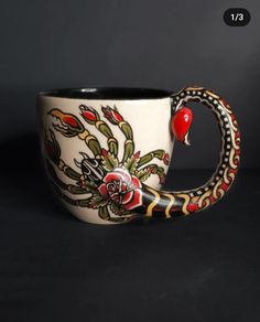 a coffee cup with a snake on it's side and a rose in the middle