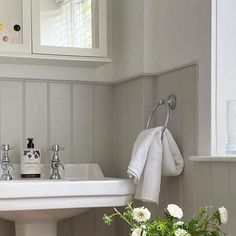 a white sink sitting under a bathroom mirror next to a vase with flowers in it