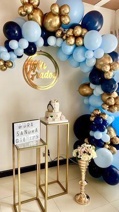 an arch made out of balloons and gold stands in front of a table with a cake on it