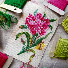 several different colored threads and spools on a table with some pink flowers