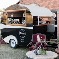 an old camper converted into a bar with flowers in the window and chairs around it