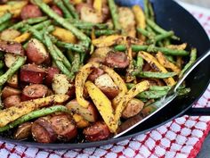 a pan filled with potatoes and asparagus on top of a red checkered table cloth