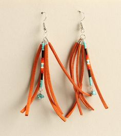 two orange tassels with beads hanging from hooks on a white surface and one has a pair of earrings attached to it