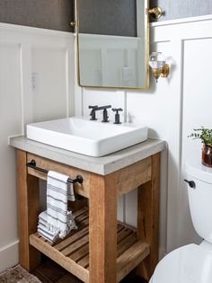 a white sink sitting under a bathroom mirror next to a wooden stand with towels on it