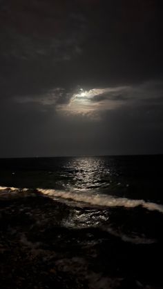 the moon is shining over the ocean on a cloudy day