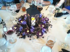 people sitting at a table with wine glasses and a lantern in the center surrounded by purple flowers