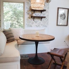 a small table with a candle on it in front of a window and some chairs