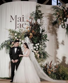 a bride and groom standing in front of a floral backdrop for their wedding ceremony at mai jade