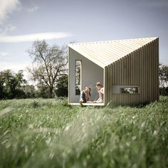 two people sitting in the window of a tiny house on grass covered field with trees