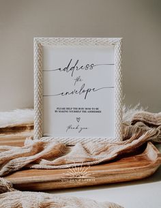 a white framed sign sitting on top of a wooden cutting board next to a blanket