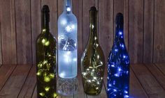 three wine bottles with lights in them sitting on a wooden table next to each other