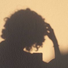 the shadow of a woman's head on a wall with a cell phone in her hand