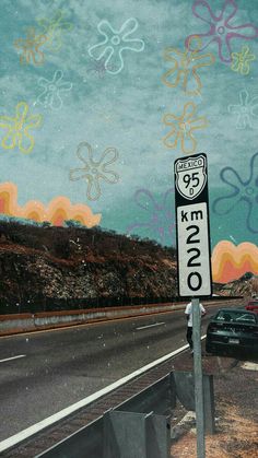 a street sign sitting on the side of a road next to a field with flowers painted on it