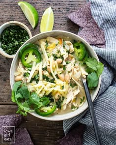 a white bowl filled with chicken, broccoli and noodles next to some tortilla chips