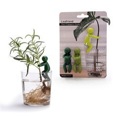 two small green figurines sitting next to a plant in a glass vase with water