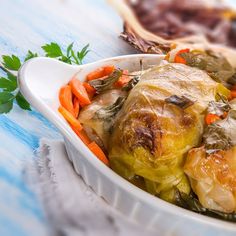 a white bowl filled with vegetables on top of a blue and white table cloth next to meat