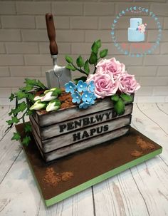 a cake with flowers and gardening tools in it on top of a wooden table next to a brick wall