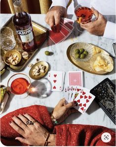 two people sitting at a table playing cards and drinking wine, with other items on the table