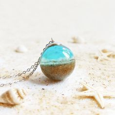 a necklace with a blue ball hanging from it's chain on the sand and starfish