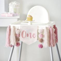 a one year old birthday banner hanging on a chair with pom - poms