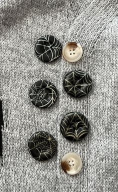 four buttons with spider webs on them sitting on top of a gray knitted sweater